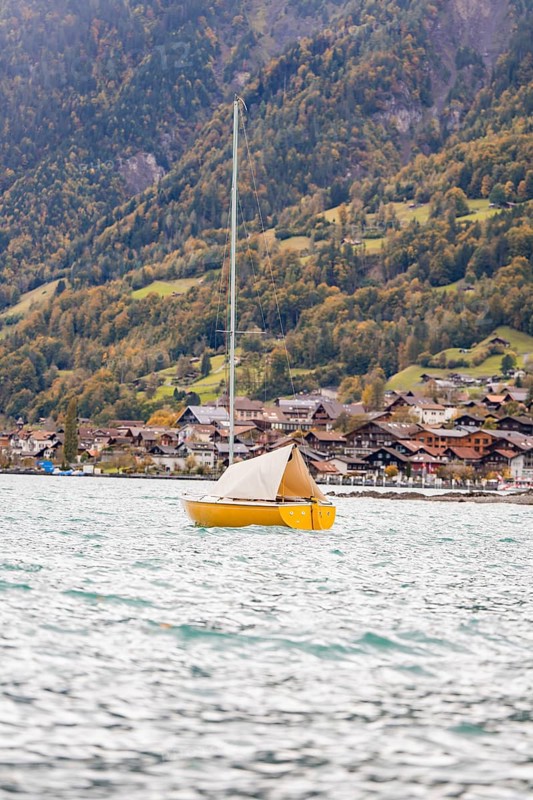 A yellow sailing boat rocks on the lake in front of a picturesque village on the mountain, Lake Brienz, Switzerland, Europe