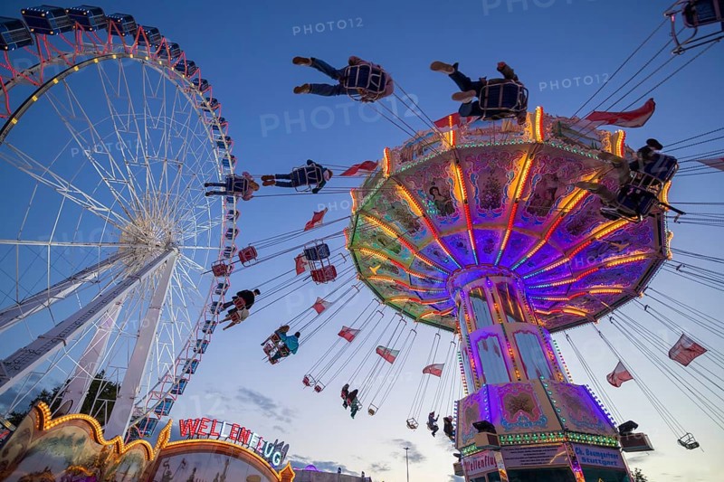A funfair at dusk with illuminated chain carousel and Ferris wheel, Europa Rad, rides, wave flight, Cannstatter Wasen, folk festival, Bad Cannstatt, Stuttgart, Baden-Württemberg, Germany, Europe
