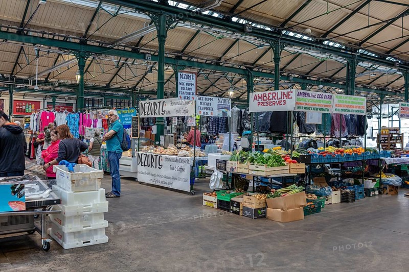 Busy indoor market filled with vegetable and clothing stalls and people, Belfast