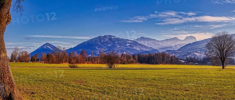 Green fields and trees in front of towering mountains under a clear blue sky, Bad Feilnbach