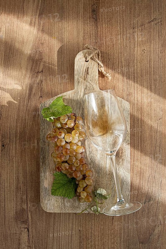A sprig of white grapes, on a wooden board, with a glass of white wine, top view, natural lighting, food concept, no people