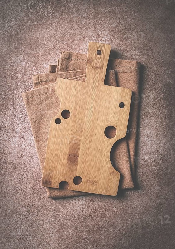 Wooden cutting board, rectangular with handle, cheese shape with holes, on a kitchen towel, top view, food background, no people