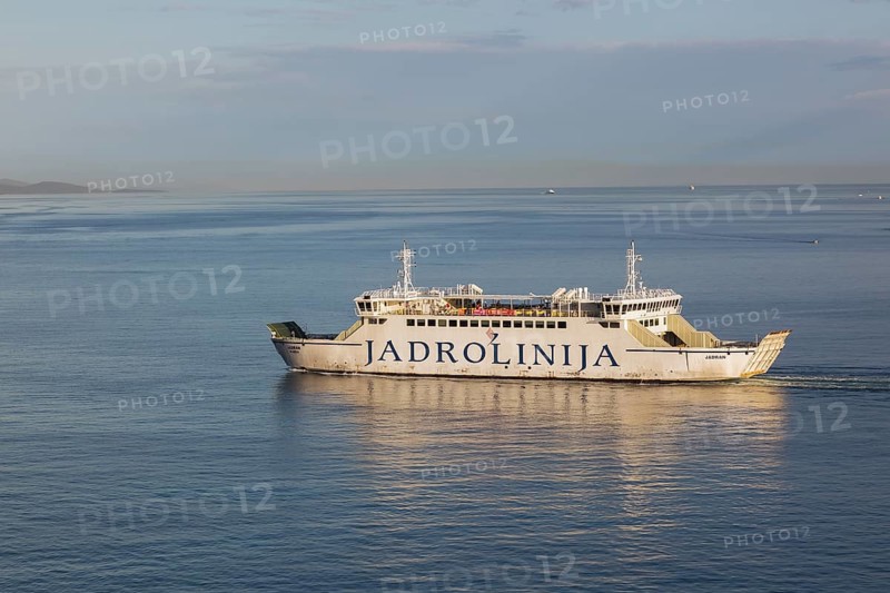 White and blue Jadrolinija Jadran Rijeka ferry boat on calm Adriatic sea leaving Port of Zadar in early morning in late summer, Croatia, Europe