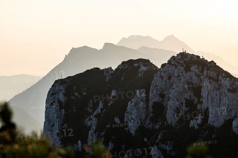 Lone mountaineer on the summit of the Hörndlwand in the Chiemgau Alps with the silhouette of Rauschberg, Zwiesel and Hochstaufen against the light in the early morning, Bavaria, Germany, Europe