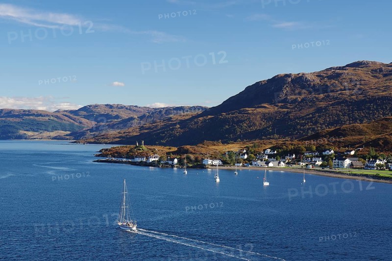 Coastal view with a sailing boat, village and hills in the background under a clear sky, autumn, October, Highlands, Kyle of Lochalsh, Scotland, United Kingdom, Europe