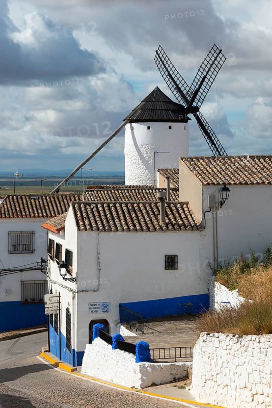 White and blue houses and windmill under a cloudy sky in a rustic village, Campo de Criptana, Ciudad Real province, Castilla-La Mancha, Route of Don Quixote, Spain, Europe