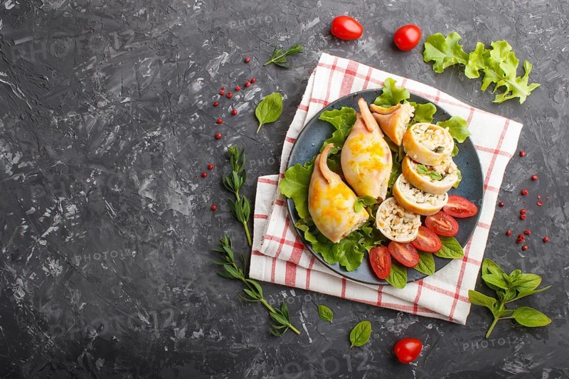 Stuffed baked squid with greens on a blue ceramic plate on a black concrete background, top view, flat lay, copy space