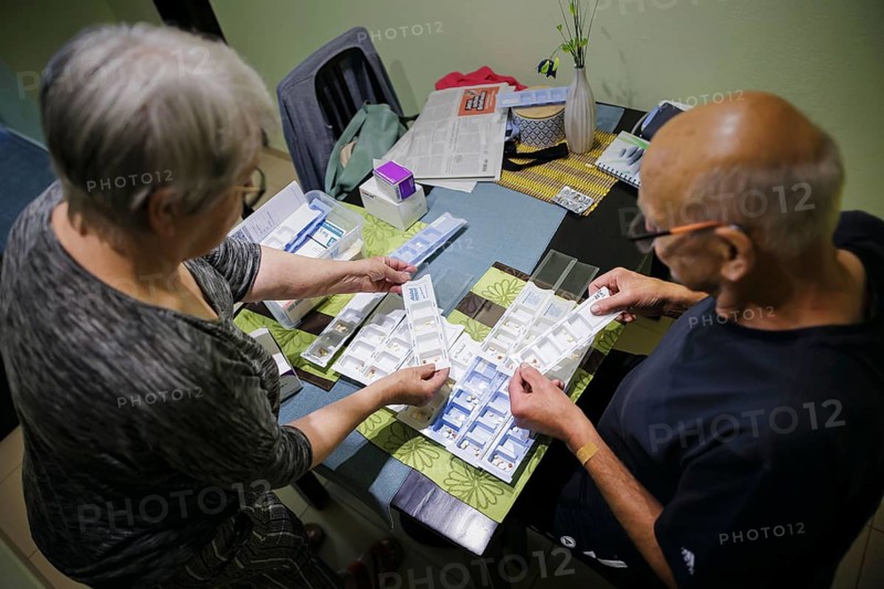 Symbolic photo on the subject of taking medication in old age. Two senior citizens sort various tablets into pill boxes at home to take for the next 16 days. Berlin, 27.07.2024
