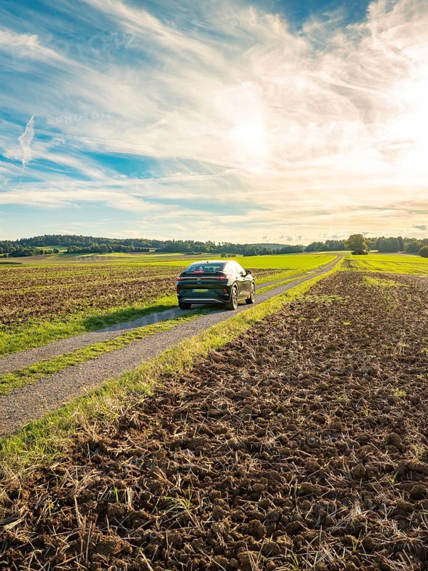 A car drives on a country lane between fields under a sky with clouds at sunset, car sharing, VW ID5, Calw, Black Forest, Germany, Europe