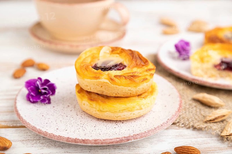 Small cheesecakes with jam and almonds with cup of coffee on a white wooden background and linen textile. Side view, close up, selective focus