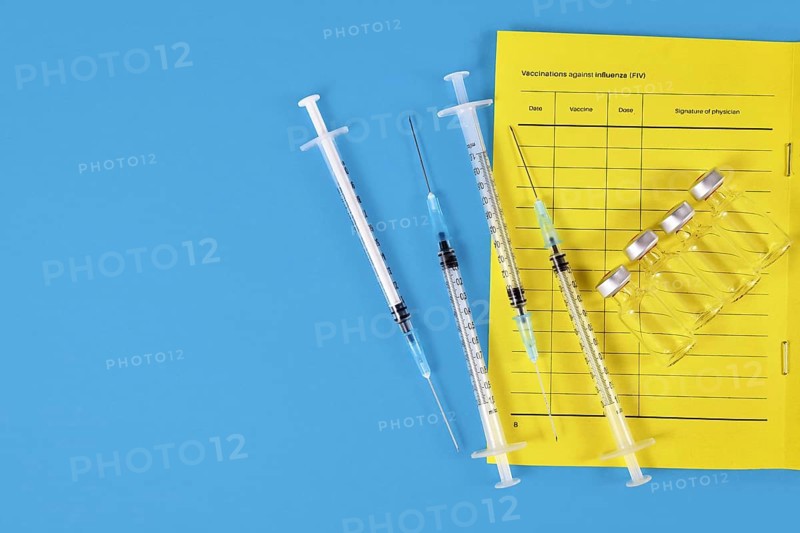 Vaccination concept with vaccine passport, 4 syringes and vials on blue background with copy space