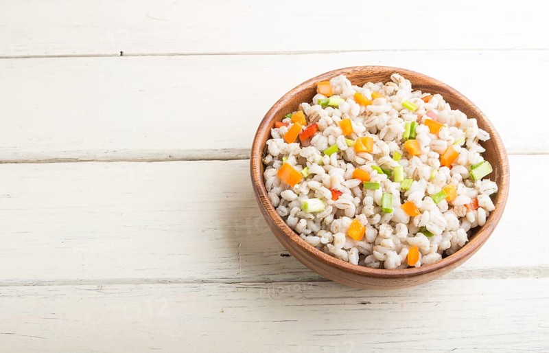 Pearl barley porridge with vegetables in wooden bowl on a white wooden background. Side view, copy space. Russian traditional cuisine
