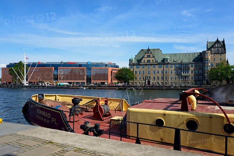 On a sunny day a boat is moored on the river in front of a city scenery with buildings, customs office, historical building, West Oder, Szczecin, West Pomerania, Poland, Europe
