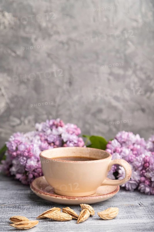 Cup of coffee with lilac and almonds on a gray wooden background. Side view, copy space. selective focus