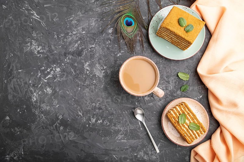 Homemade honey cake with milk cream and mint with cup of coffee on a black concrete background and orange textile. top view, flat lay, copy space