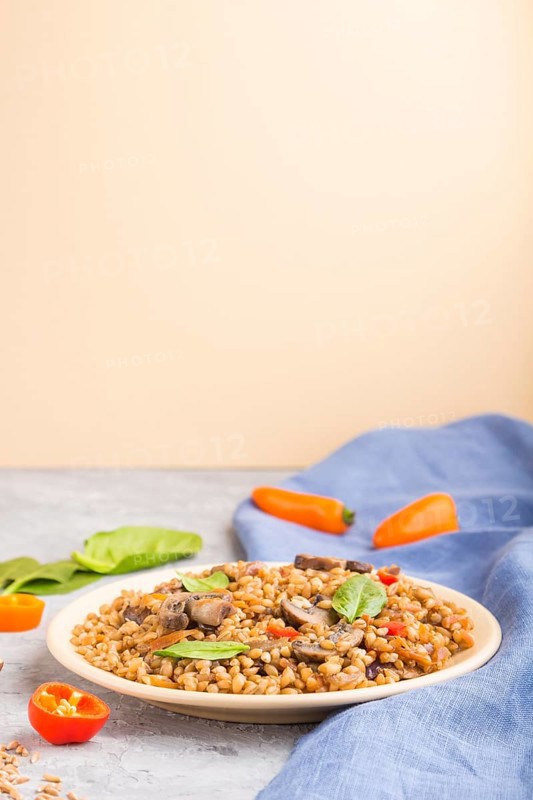 Spelt (dinkel wheat) porridge with vegetables and mushrooms on ceramic plate on gray and orange background and blue linen textile. Side view, copy space, selective focus. Russian traditional cuisine