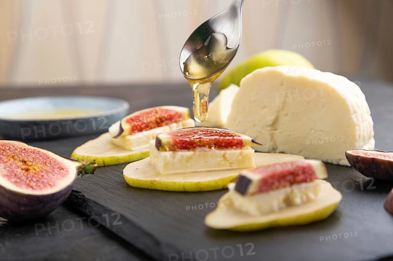 Summer appetizer with pear, cottage cheese, figs and honey on slate board on a black concrete background. Side view, close up, selective focus