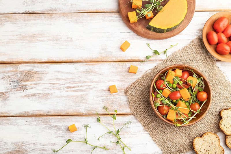Vegetarian vegetable salad of tomatoes, pumpkin, microgreen pea sprouts on white wooden background and linen textile. Top view, flat lay, copy space