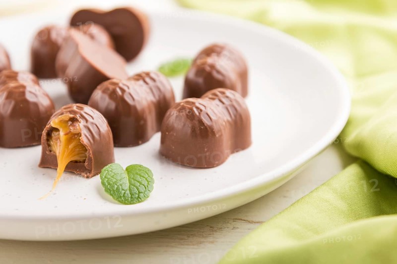 Chocolate candies with almonds and caramel on a white wooden background and green textile. side view, close up, selective focus