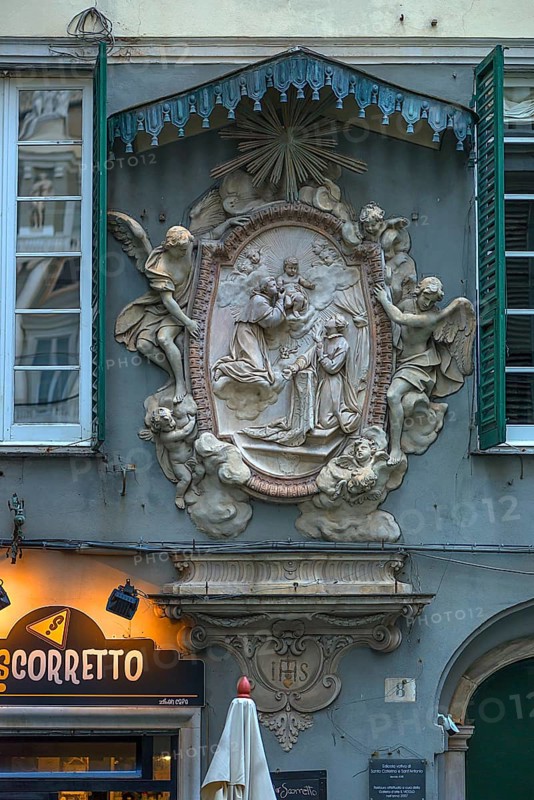 Relief group of saints and angel sculptures under a canopy on a residential building in the historic centre, Genoa, Italy, Europe