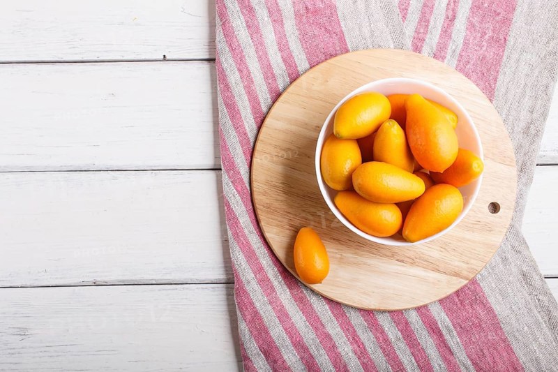 Kumquats in a white plate on a white wooden background, top view, flat lay, copy space
