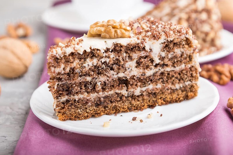 Homemade cake with milk cream and walnuts with cup of coffee on a gray concrete background and purple textile. side view, close up, selective focus