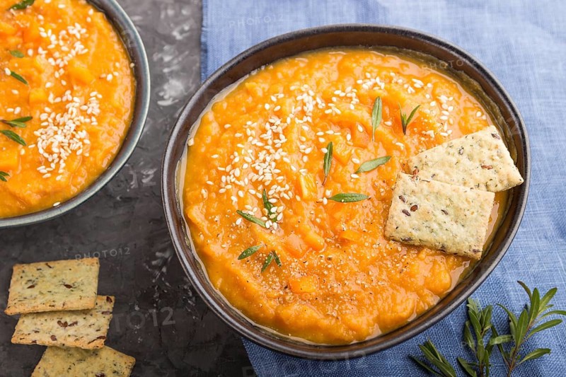 Sweet potato or batata cream soup with sesame seeds and snacks in blue ceramic bowls on a black concrete background with blue linen textile. top view, close up, selective focus