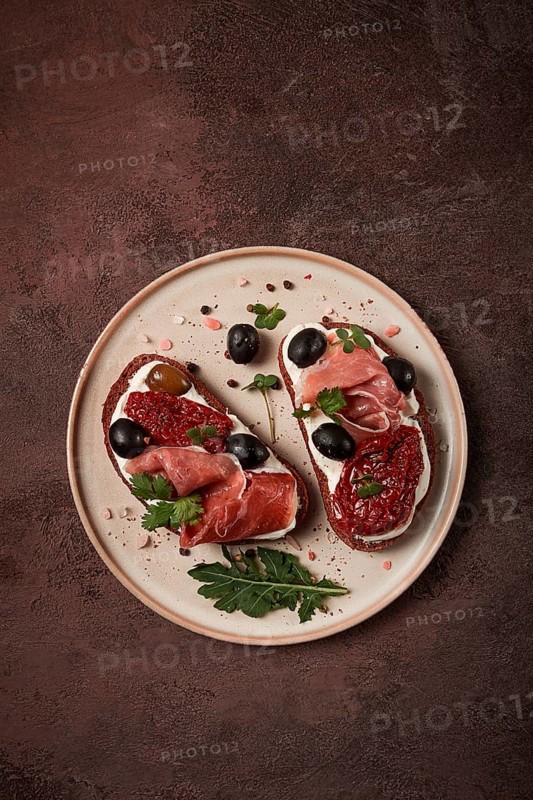 Sandwiches with cheese and prosciutto, dried tomatoes and olives, breakfast on a plate