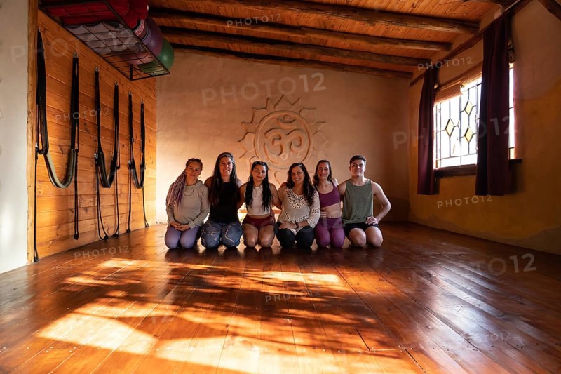 Group portrait of a community of people practicing yoga smiling and looking at the camera. General shot illuminated with natural light coming in through side windows