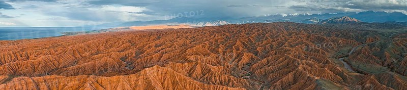 Panorama, landscape of eroded hills, badlands at sunset, behind mountain peaks of the Tian Shan Mountains and Issyk Kul Lake, aerial view, Canyon of the Forgotten Rivers, Issyk Kul, Kyrgyzstan, Asia