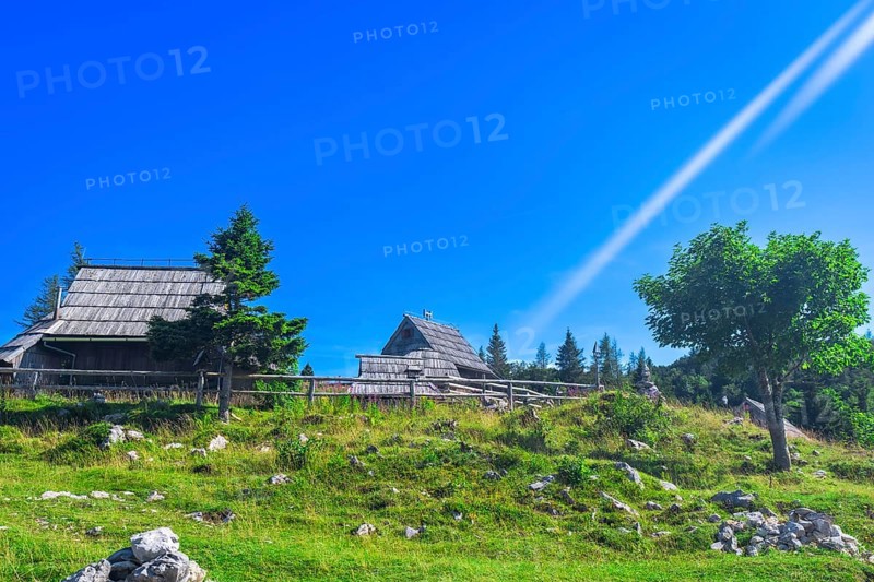 Scenic view of idyllic wooden huts on velika planina plateau with lush green meadows and clear blue sky, showcasing traditional slovenian architecture