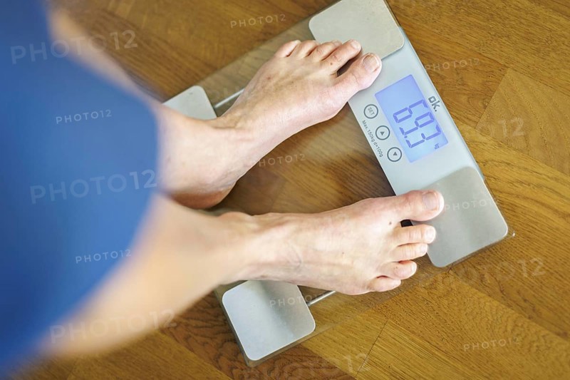 Symbolic photo on the subject of body weight. The feet of a 60-year-old person can be seen next to the weight display of a scale. Berlin, 13.08.2024