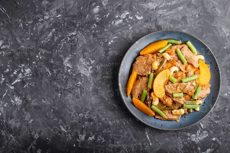 Fried pork with peaches, cashew and green beans on a black concrete background. Top view, copy space, flat lay. chinese cuisine