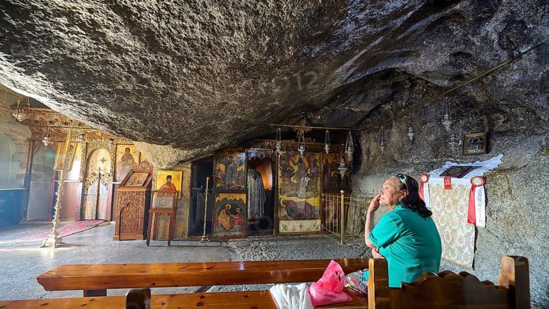 Interior view of a church with a woman praying on a wooden bench and religious art, rock grotto, Monastery tis Apokalipsis, Patmos, Dodecanese, Greek Islands, Greece, Europe