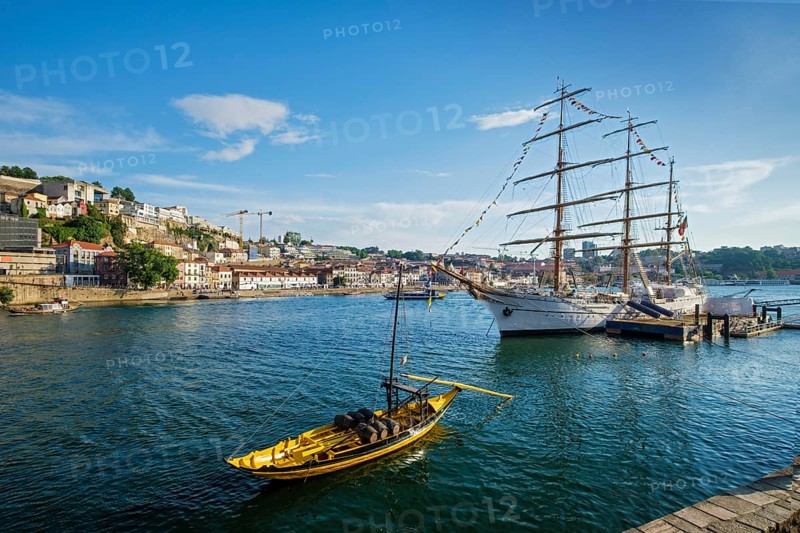 View of Vila Nova de Gaia city with sailing ship and traditional boat with port wine barrels and Douro river with tourist boats on sunset. Porto, Portugal, Europe