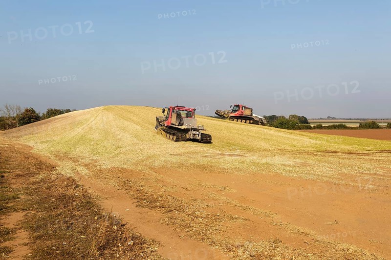 Piston Bully tracked bulldozer vehicles building silage clamp of sweetcorn maize in field stored for biofuel, Alderton, Suffolk, England, UK