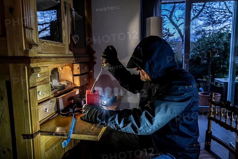 Symbolic image of a burglary, perpetrator has broken into a flat from the garden side and is looking for loot, breaks open a cash box, valuables, money