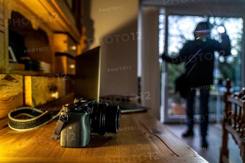 Symbolic image of a burglary, perpetrator has broken into a flat from the garden side and is looking for loot, computer, laptop, valuables, money, technology