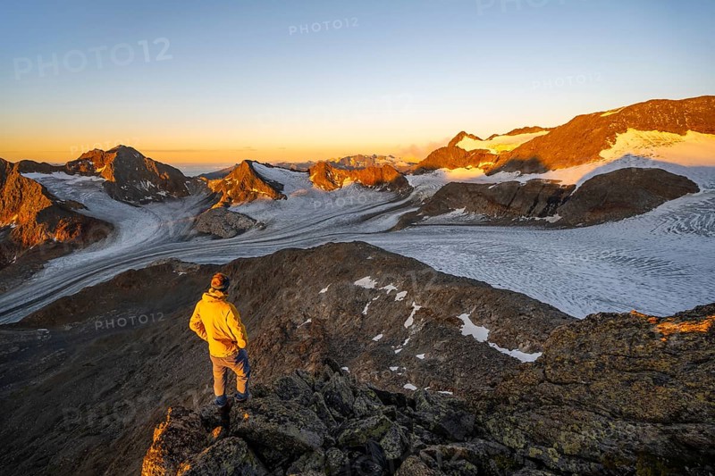 Mountaineer at the summit of the Becher, view of high mountain landscape with glacier Übeltalferner, alpenglow at sunrise, Stubai Alps, South Tyrol, Italy, Europe