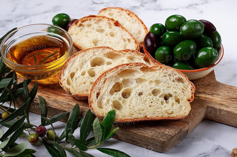 Appetizer, sliced ciabatta bread, with olive oil, green olives, Chalkidiki olives, classic Green green olive, on a marble table, top view, no people