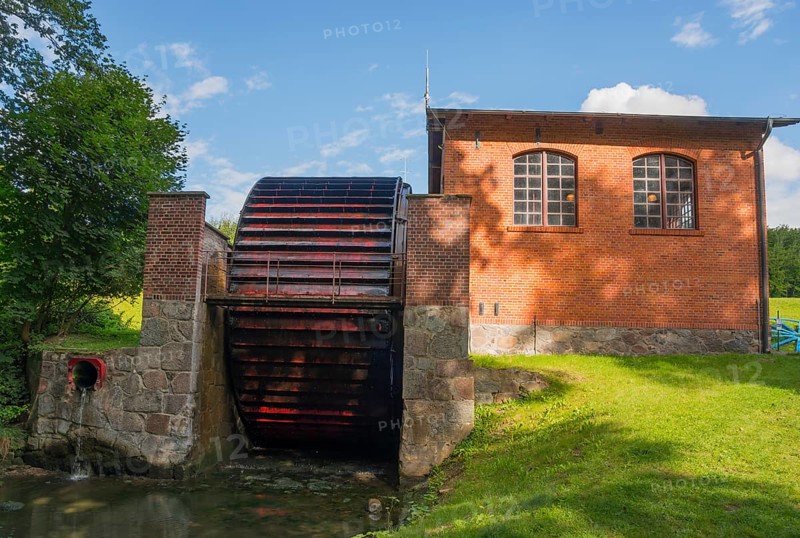 A large waterwheel next to a brick building in a green setting, engine house with waterwheel to drive the cable drum, Upland Canal, Warminsko-Mazurskie, Warminsko-Mazurskie, Poland, Europe