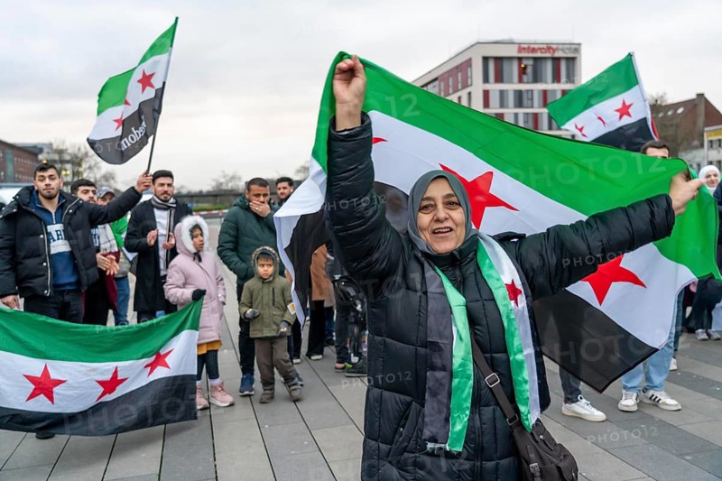 Syrian woman celebrate the end of the Assad regime after the change of power in Syria at a rally on the square in front of the main railway station in Duisburg, North Rhine-Westphalia, Germany, Europe