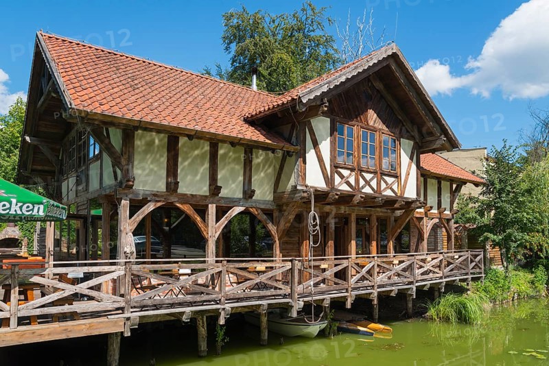 Half-timbered house with terrace by the water, surrounded by green nature and blue sky, Restaurant Tawerna, Ostroda, Osterode in East Prussia, Warminsko-Mazurskie, Poland, Europe