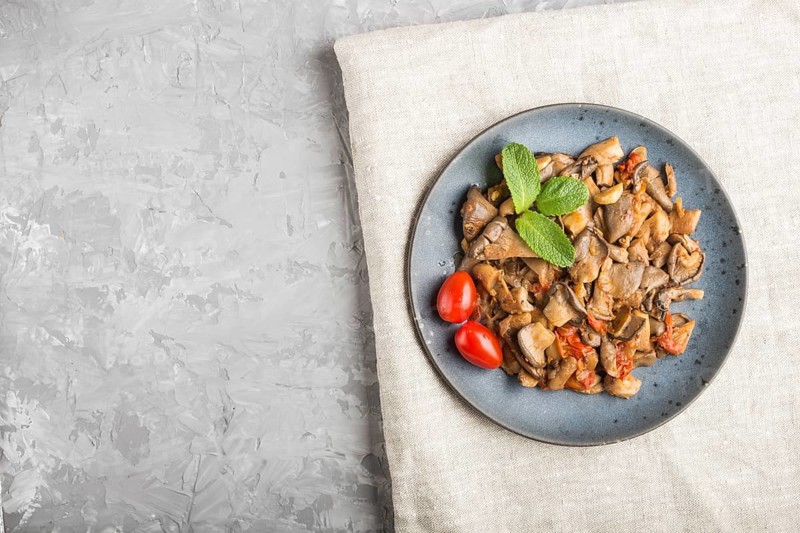Fried oyster mushrooms with tomatoes on gray concrete background. Top view, copy space
