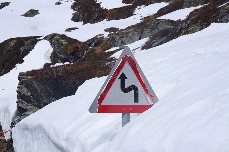 Traffic sign on a snow-covered mountain road indicating a sharp bend, June, Geiranger, Fjordland, Norway, Europe