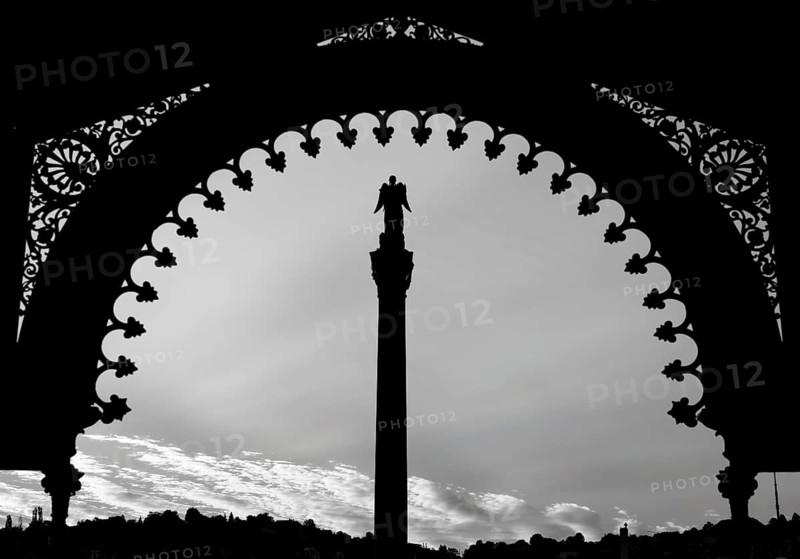 A statue stands on a pillar under a richly decorated archway