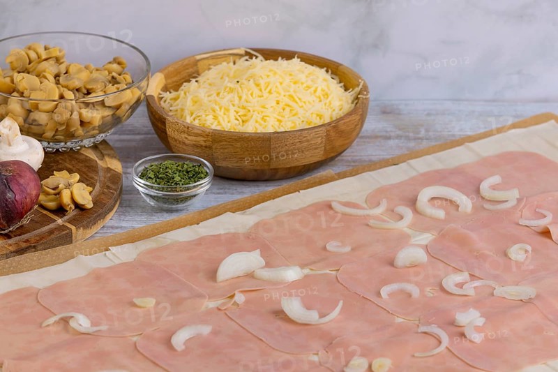 Ingredients such as cheese, onions, mushrooms next to strudel dough topped with ham