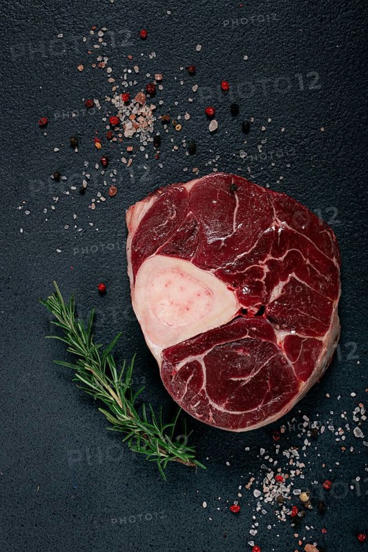 A shank on the bone, raw meat for ossobuco, on the table, with a branch of rosemary, top view, no people