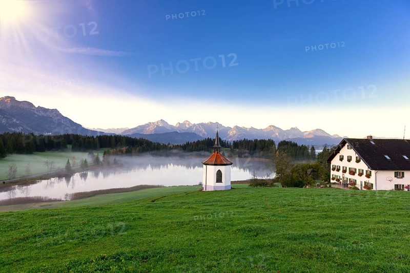 Landscape with lake, small chapel and house in the morning sunlight, framed by mountains and meadow, Hegratsrieder See near Füssen, Ostallgäu, Allgäu, Bavaria, Germany, Europe