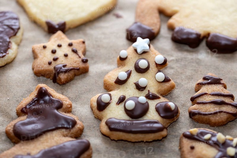 Festive biscuits with chocolate decorations in the shape of Christmas trees and stars on baking paper, Christmas baking, Christmas biscuits, Germany, Europe